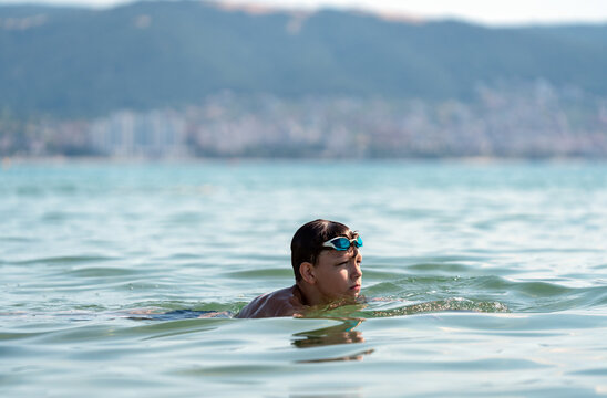 Teenage swimmer in calm open sea during a summer outdoor training session. Healthy active lifestyle, open water swimming, youth sport and outdoor recreation by the coast.