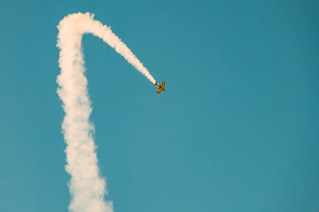 Portugal Oeiras Air Show.  A stunt plane makes a loop in the sky while leaving a smoke trail. The scene shows a clear blue sky with the aircraft performing tricks for an audience below. © SValeriia