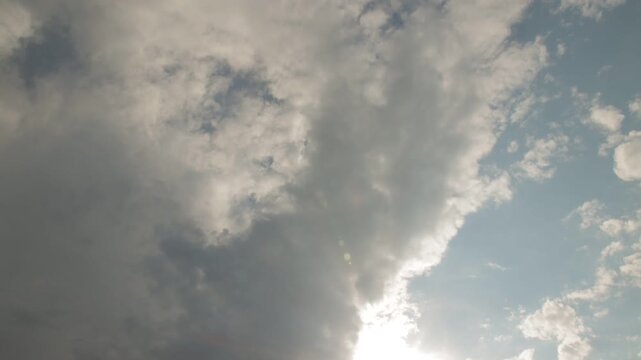 Time-lapse of thick white and gray clouds moving across blue sky with sunlight breaking through