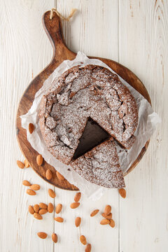 Torta Caprese highlighting the texture of the chocolate and almond cake, topped with powdered sugar closeup on the wooden board on the table. Vertical top view from above