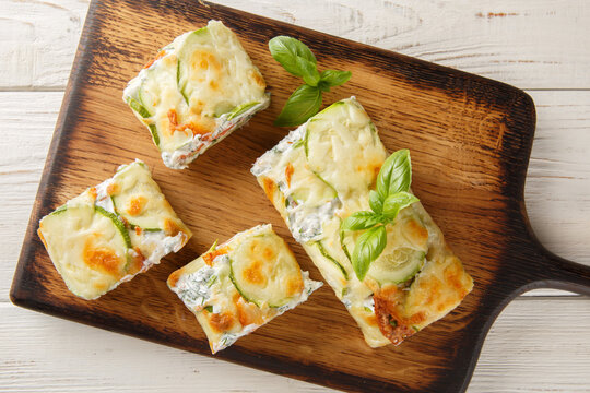Appetizer Roll of sliced ​​zucchini stuffed with salmon and cream cheese close-up on a wooden board on the table. Horizontal top view from above