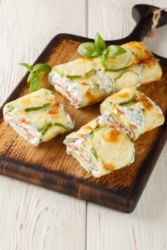 Baked Zucchini roll with cream cheese, herbs and salmon closeup on the wooden board on the table. Vertical