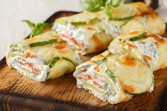 Close-up of sliced ​​zucchini roll stuffed with salmon and cream cheese on a wooden board on the table. Horizontal