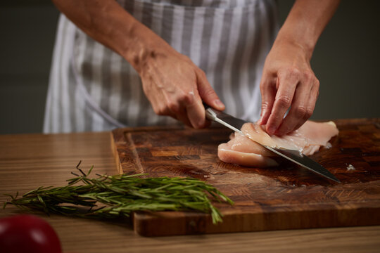 Chef slicing raw chicken breast on wooden board