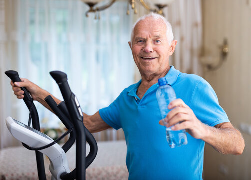 Elderly sporty man exercising on an elliptical trainer and drinking water from bottle