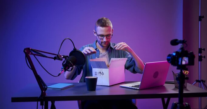 Man unpacking a product box while recording video at desk with camera and microphone