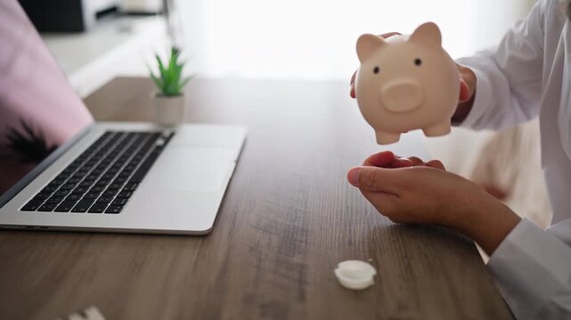 Close up view of a man's hands holding and shaking an empty piggy bank at his office desk, symbolizing bankruptcy, poor financial management, economic crisis, and no available funds