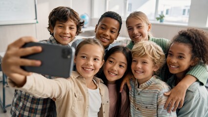 Obraz premium Diverse elementary school children taking a smartphone selfie together in a bright classroom, smiling at the camera and showing friendship, teamwork and cheerful back to school life