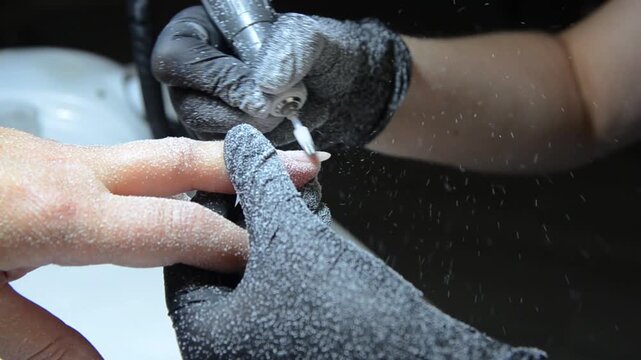 Close-up of a professional nail technician removing old gel polish with an electric nail drill and ceramic drill bit during a manicure procedure.