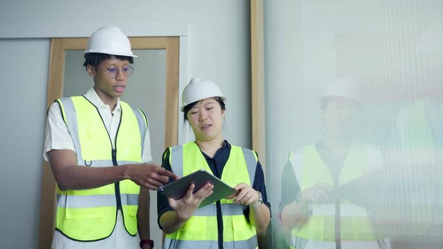 Diverse construction engineers holding digital tablet and pointing away during inspection at modern building site