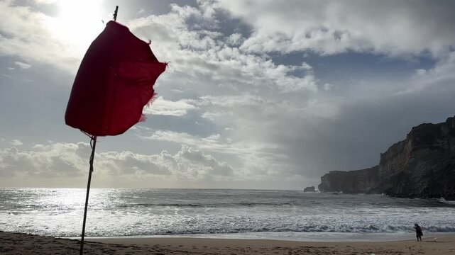 Red warning flag on windy beach with dramatic sky and ocean waves