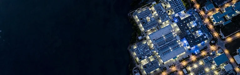 Aerial top-down night view of an illuminated tech facility and data center campus along a waterfront with copy space © King22