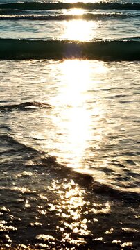 Primer plano cinem&aacute;tico de suave ola marina con espuma cubriendo la arena dorada, con deslumbrantes reflejos del sol dorado sobre el agua turquesa al atardecer.