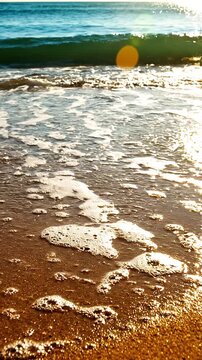 Primer plano cinem&aacute;tico de suave ola marina con espuma cubriendo la arena dorada, con deslumbrantes reflejos del sol dorado sobre el agua turquesa al atardecer.