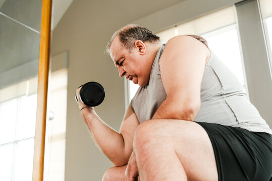 Adult exercising indoors, performing a bicep curl with a dumbbell near a window, showing focus and effort in a home workout