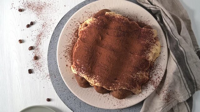 Overhead flat lay of an Italian tiramisu dessert on a plate, featuring soft lighting and a textured surface dusted with cocoa powder and scattered coffee bean