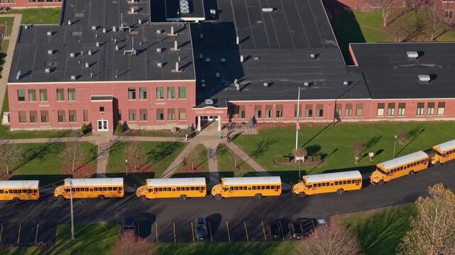 Drone view of yellow school buses waiting outside an American school during dismissal time