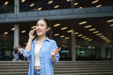 Fototapeta premium portrait of cheerful asian female student talking on cellphone, walking in university campus outdoors, looking around, Education in high school university college concept