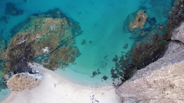 Aerial drone view of tourists on Playa de Los Muertos beach in Cabo de Gata, Almeria, Spain revealing a stunning turquoise sea