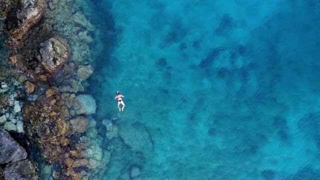 Drone's aerial view of woman swimming on her back in turquoise sea water at Los Muertos Beach, Cabo de Gata, Spain