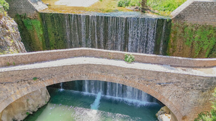 Aerial close up view of an old stone bridge span in front of a cascading waterfall curtain and green mountain gorge in Paleokaria Thessaly Greece © moryachka
