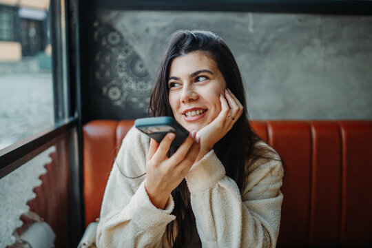 Woman smiling recording voice message on smartphone in cafe