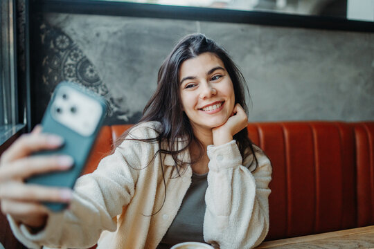 Woman smiling while taking selfie with smartphone in cafe