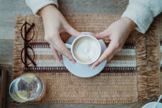 Woman's hands holding coffee cup on cozy placemat