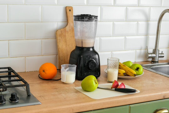 Electric blender on kitchen counter for smoothie making process. Fresh fruits, cutting board, and glass of protein milkshake on table. Healthy lifestyle. Vitamin Boost, Morning Routine and Self Care