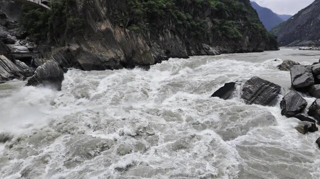 Turbulent River in Gorge with Arch Bridge and Boulders