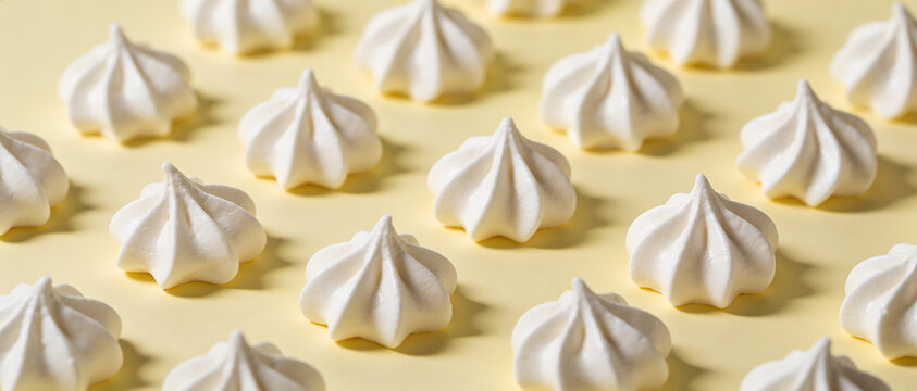 Rows of sweet white meringue cookies arranged in a neat pattern on a pastel yellow background.