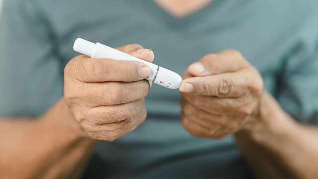 Close-up of a senior adult using a lancet device for finger prick blood glucose testing at home. Diabetes self-monitoring supports preventive healthcare, chronic disease management.