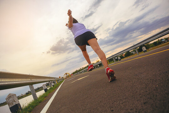 Silhouette of young woman running sprinting on road. Fit runner fitness runner during outdoor workout with sunset background