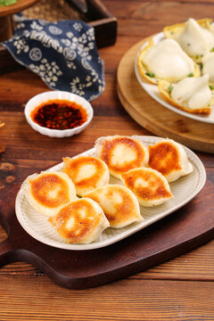 Golden Pan-Fried Chinese Dumplings with Crispy Bottom and Dipping Sauce on Rustic Wooden Table