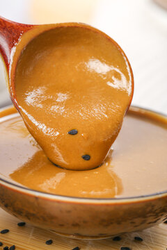 Traditional Henan Sesame Hot Sauce Pouring from Wooden Ladle into Bowl for Dipping