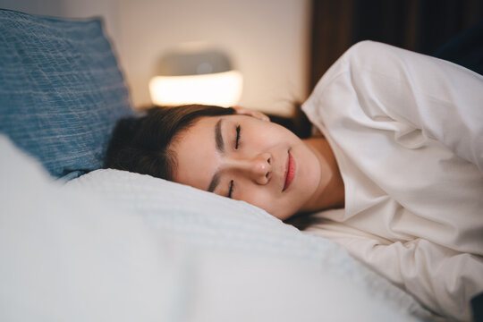 Attractive young adult asian woman close eye sleep in soft bed relax lying in bedroom on nigh