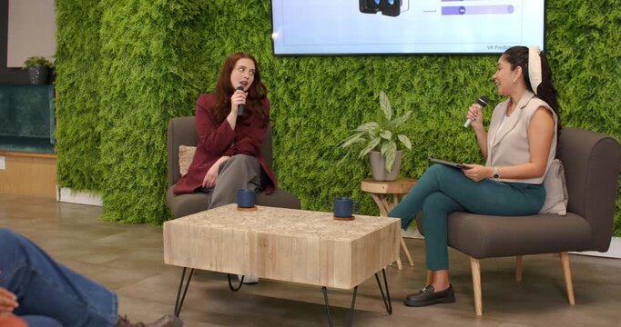 Female host asking product questions onstage, guest replying lively holding mic, host with tablet