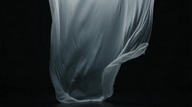 Graceful white fabric flows and dances elegantly against a stark black backdrop, creating fluid, ethereal shapes in slow motion.