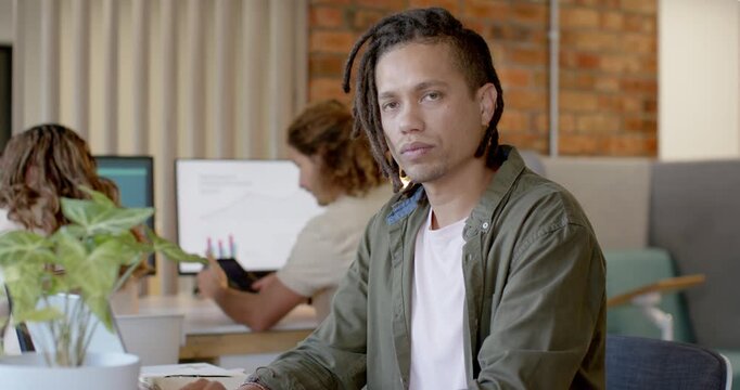 African American man typing keyboard at office, glancing at tablet, smiling at camera in olive tee