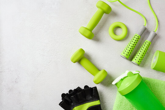 Green sports accessories and dumbbells on light concrete background flatlay