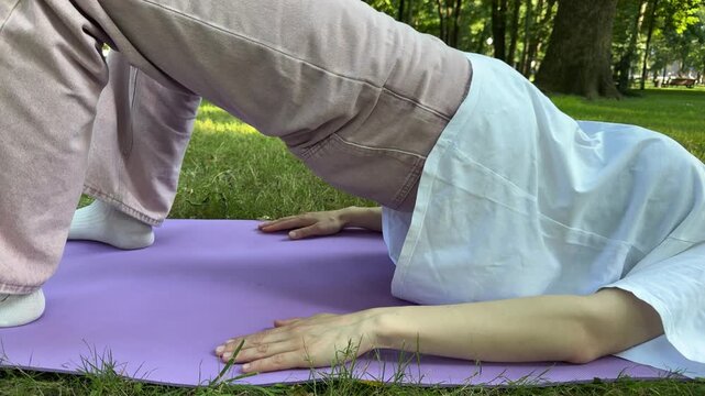 Woman doing glutes and hamstrings exercise on purple mat in park, outdoor fitness workout, stretching, healthy lifestyle, white tshirt