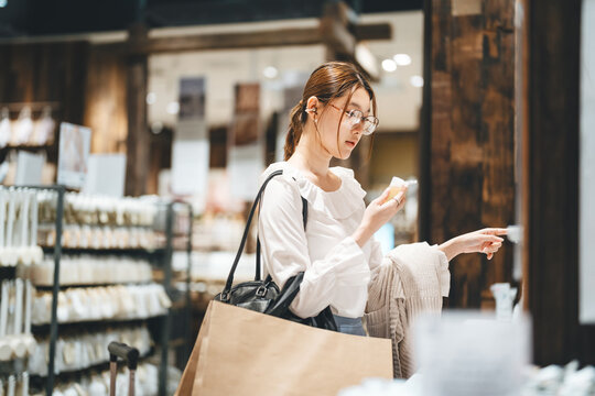Young adult asian woman shopping facial skin care choosing beauty product in retail store japanese business look fashion