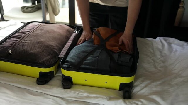 Close up of male hands carefully unzipping and opening a bright yellow hard-shell suitcase on a white bed. Unpacking clothes and baggage after vacation, arriving at a hotel room, or returning home