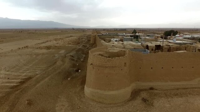 Spectacular drone perspective capturing a massive ancient mud citadel within a quiet desert village background, revealing historic clay castle walls and middle eastern heritage assets.