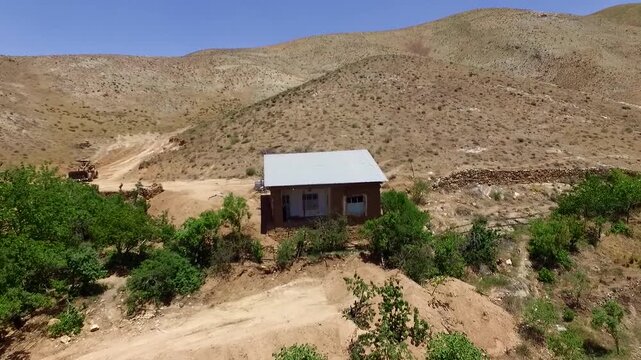 Fascinating close-up aerial shot focusing on a traditional rustic house building built on a dry rocky mountain slope, capturing remote village architectures and simple country lifestyle.