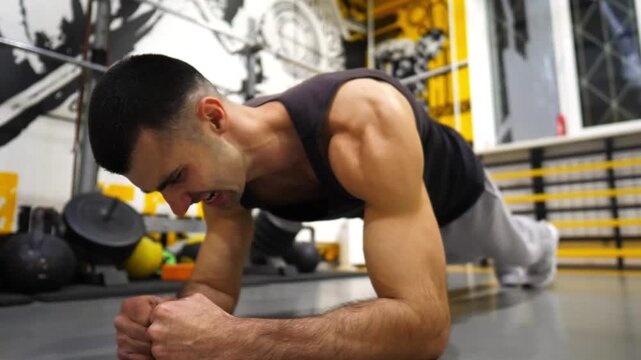 Strong sporty man doing a plank at modern gym. Young muscular sportsman strengthens his abdominal muscles at sport club. Athletic guy training in fitness centre. Concept of healthy lifestyle. Close up
