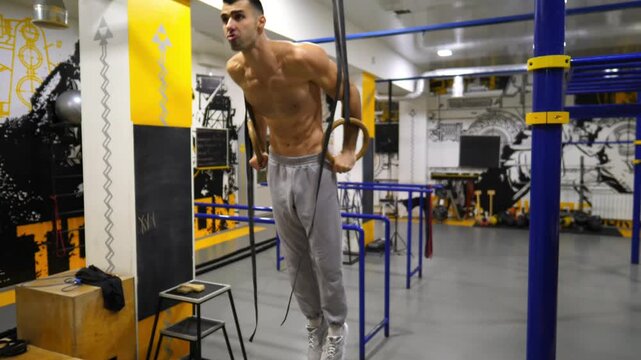Strong athlete doing push ups on gymnastic rings at modern gym. Muscular shirtless sportsman exercising hard at fitness club. Young male gymnast training indoor. Healthy and active lifestyle concept