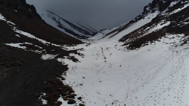 Spectacular uav shot hovering over a deep mountain pass filled with pristine winter snow, highlighting majestic alpine slopes and frozen nature during a chilly overcast afternoon track.