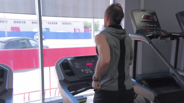 Man exercises on treadmill in gym located in city during midday hours