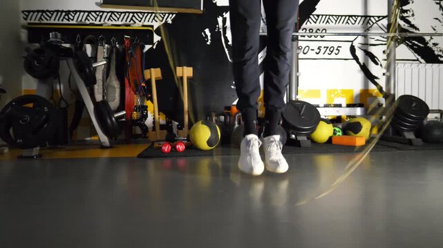 Legs of young sportsman skipping with a jump rope at sport club. Male feet of athlete exercising in fitness centre. Sporty man in sportswear doing cardio at modern gym. Concept of active lifestyle